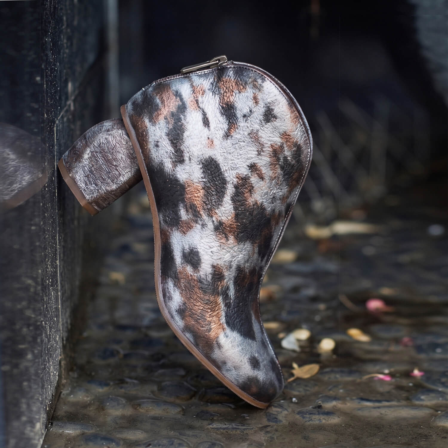 Light gold mottled metallic ankle bootie with a sculpted block heel against a dark metal grate